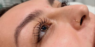 Close-up of a person's face lying down, showing long eyelashes, clear skin, and a nose ring.